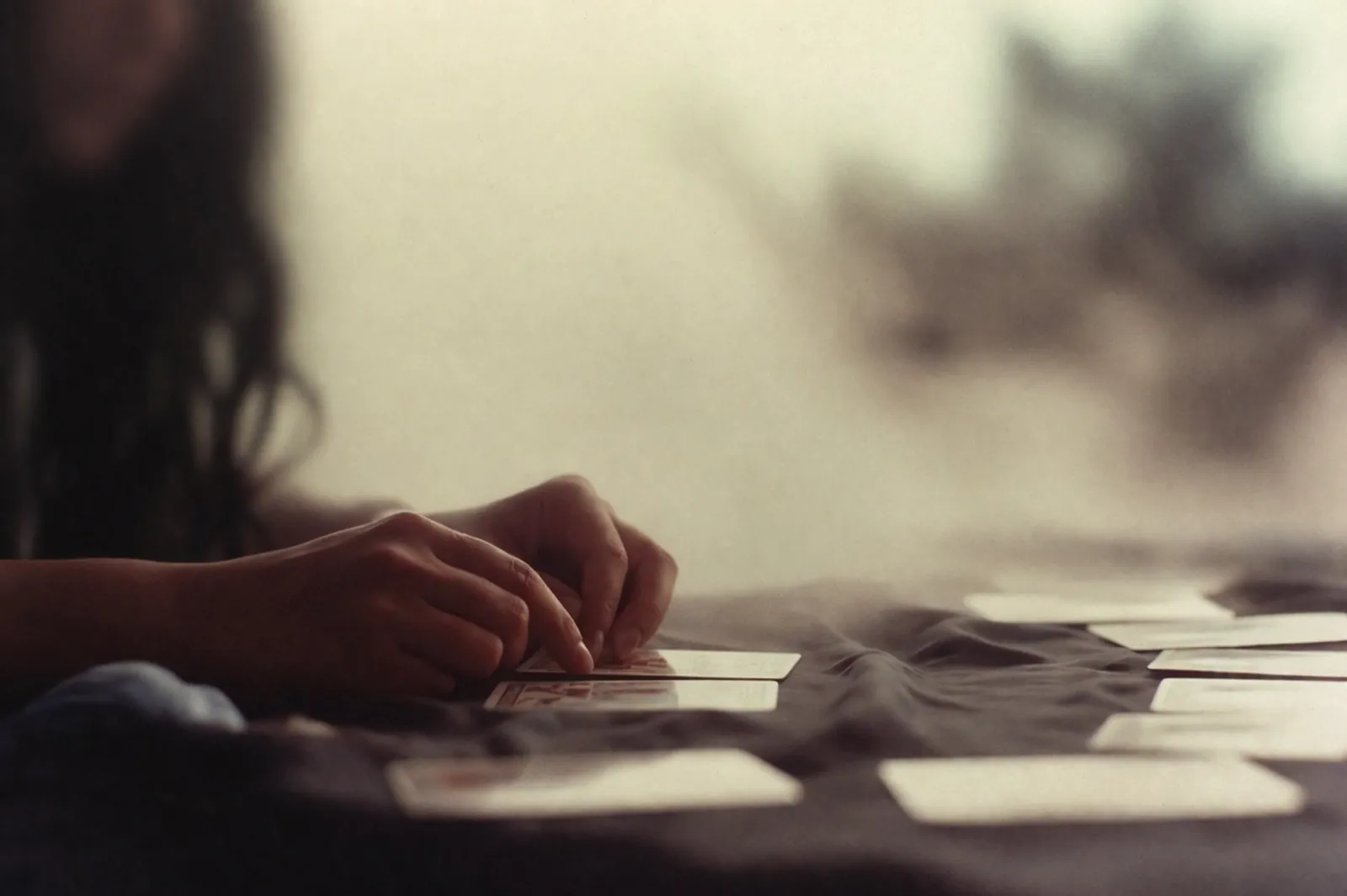 Hände beim Legen von Tarotkarten auf dunklem Stoff in weichem, altfilmischem Licht