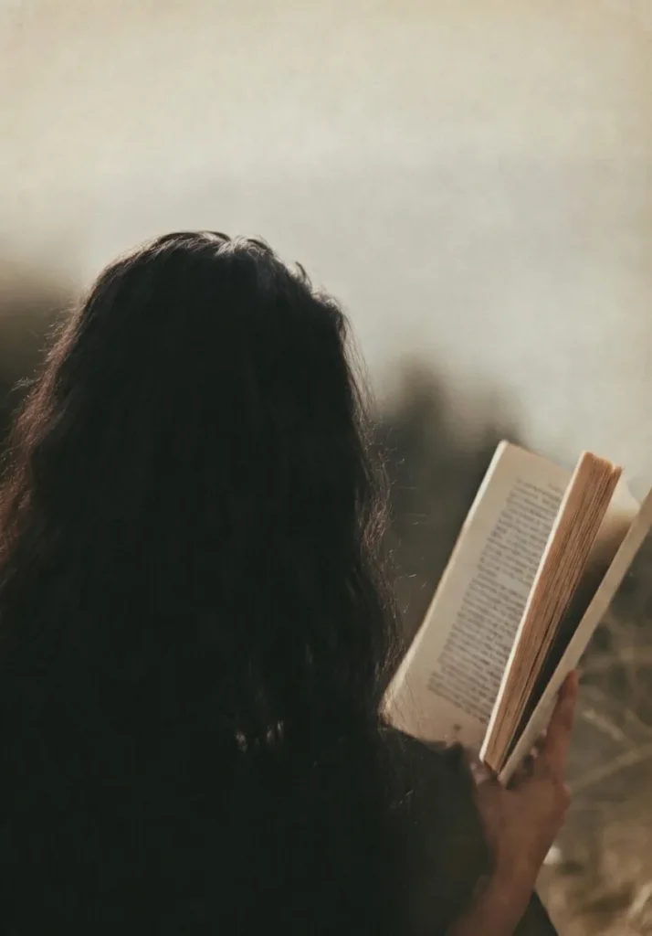 Frau mit langem dunklem Haar liest in warmem Licht in einem offenen Buch